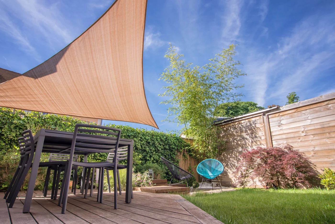 Sail shade over a dark wood outdoor table in St. Helena, CA yard by The Home Living Company