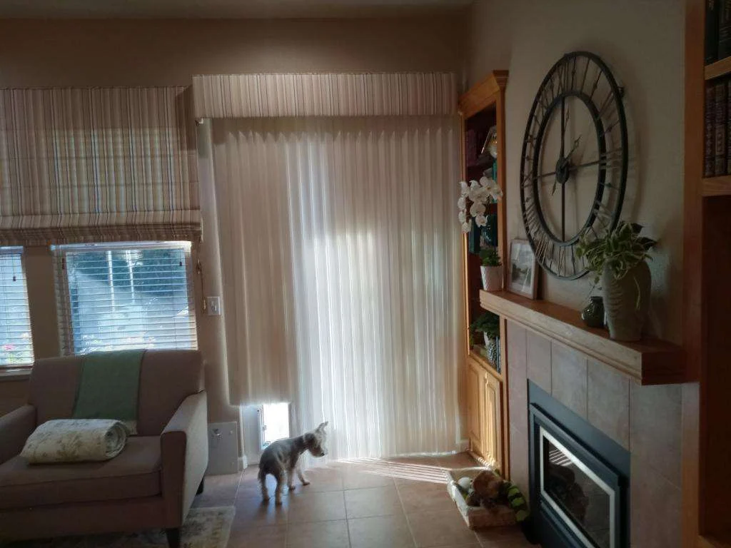 Pro Drapery Installation | Lafayette, CA | Home Living Window Fashions Image of a tan living room with a sliding glass patio door covered with off-white fabric, vertical blind drapery